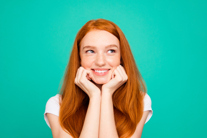 Portrait of charming, lovely, cute, beautiful, sweet lady look aside touch cheeks by hands fists and smile isolated on pastel turquoise background